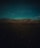 Rolling hills under a twilight sky with a solitary figure tending to a herd of animals in the foreground. The landscape is dimly lit, accentuated by the shadows that stretch across the terrain.