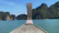 Small boat gliding over calm turquoise waters with jungle cliffs in the distance under a sunny sky.
