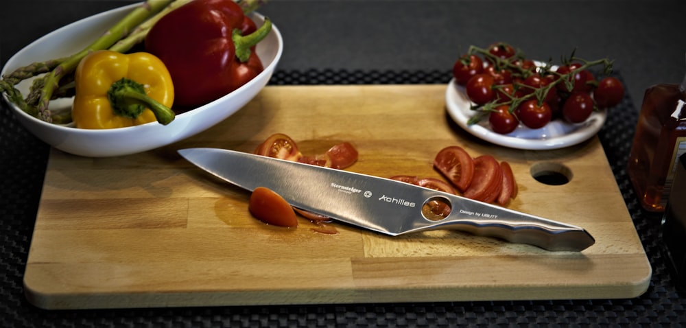 a cutting board topped with a knife and a bowl of vegetables