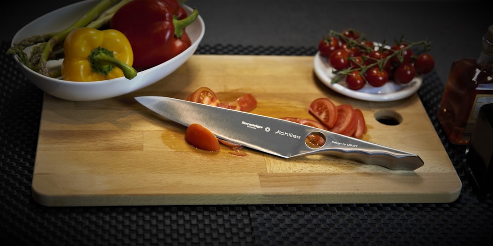 a cutting board with a knife and a bowl of tomatoes