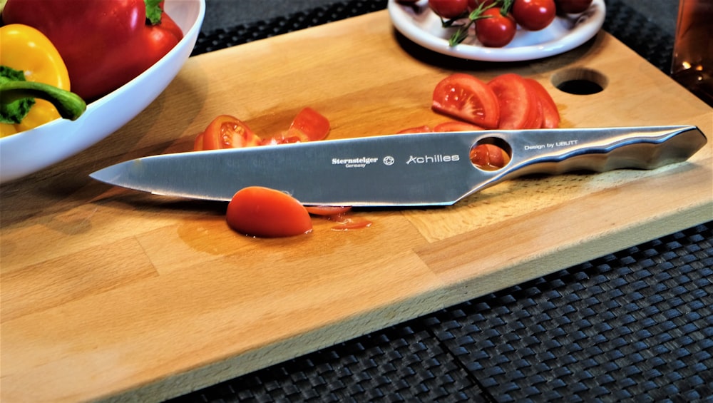 a knife on a cutting board next to a bowl of tomatoes