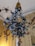 A decorative floral arrangement is hanging from the ceiling, featuring intricately designed white roses with green leaves set against a lavish, ornately decorated background. The background has golden hues with additional floral motifs, enhancing the luxurious ambiance.