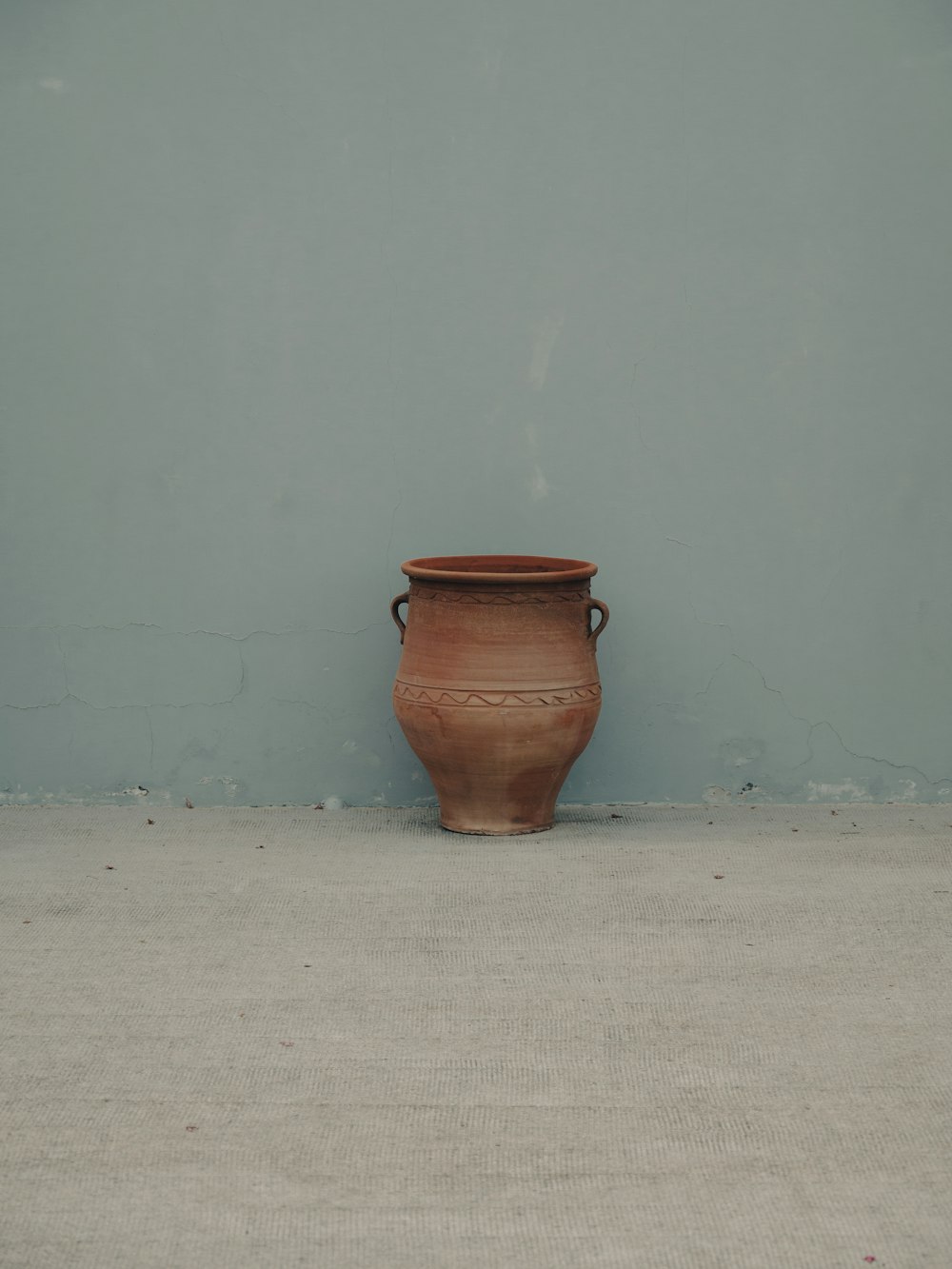 a brown vase sitting on the ground in front of a blue wall