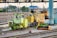 Numerous maintenance vehicles and equipment are stationed on railway tracks. The area appears to be an industrial or depot setting with multiple rail lines converging. Various colors of machinery, predominantly yellow and green, are visible, and some construction or maintenance materials are scattered nearby.