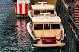 Two medium-sized boats with beige canopies are docked next to a pier. A red and white-striped buoy is visible on the left, and a set of stairs is on the right.
