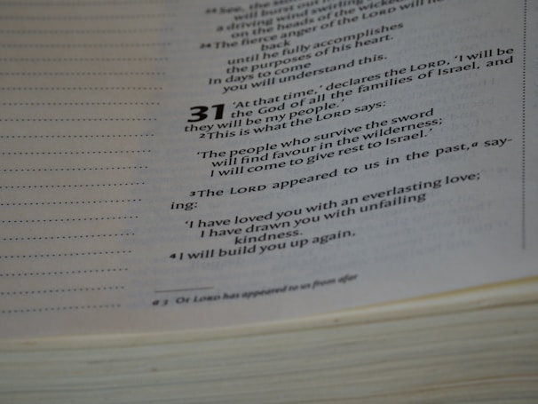 A close-up view of an open book displaying text from a religious or spiritual scripture with numbered verses. The text is formatted with bold numbers indicating specific sections or verses, and includes phrases referencing divine declarations.