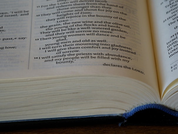 An open book with visible text featuring a passage from the Bible. The pages are slightly curved, and the book's cover is blue. The focus is on the central section of the text.