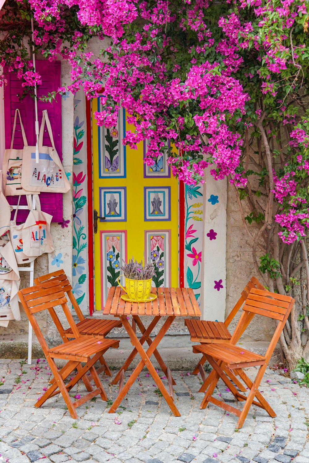 Una mesa de madera con cuatro sillas bajo un árbol de bougaia rosa