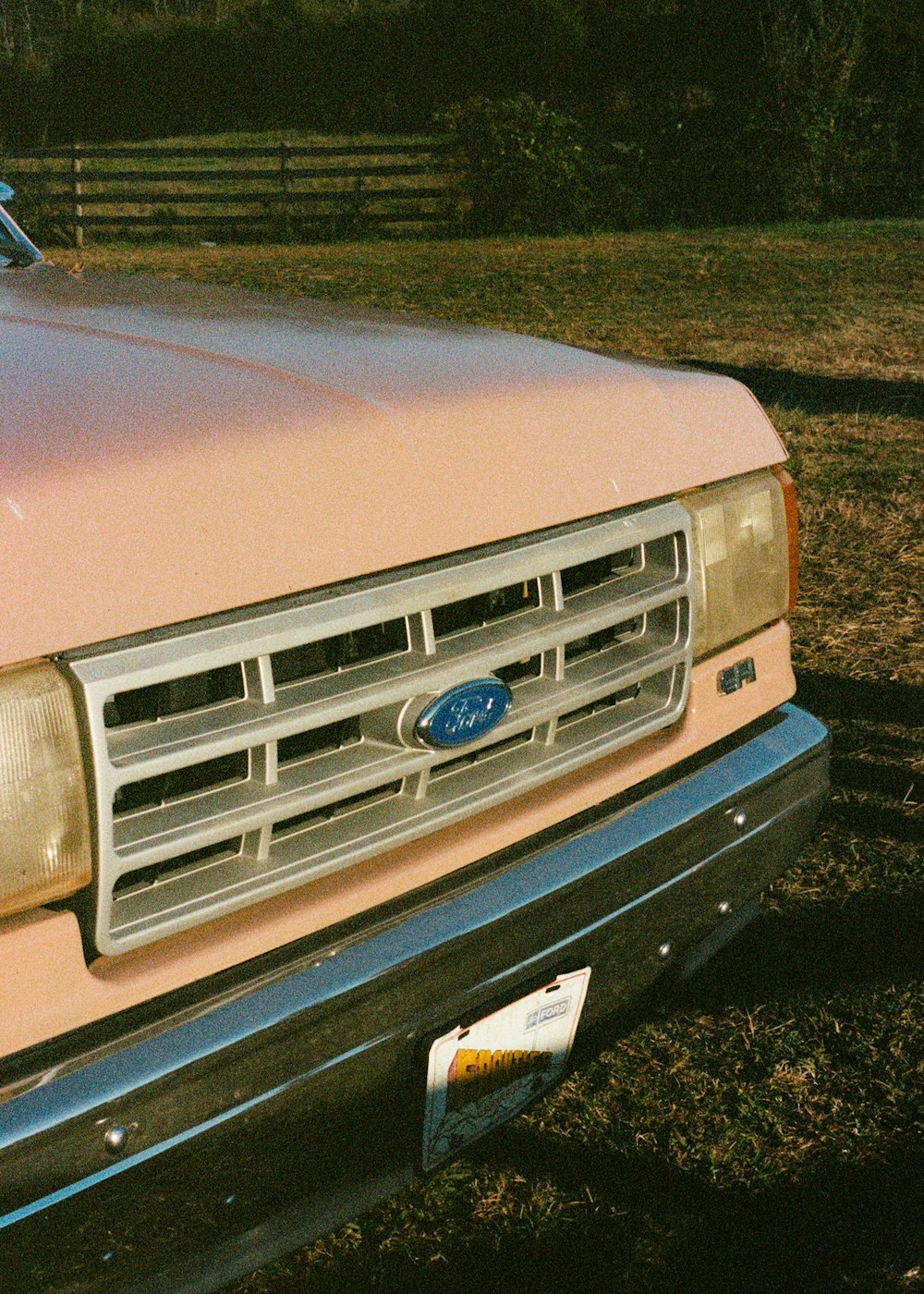 a pink truck parked in a field next to a fence