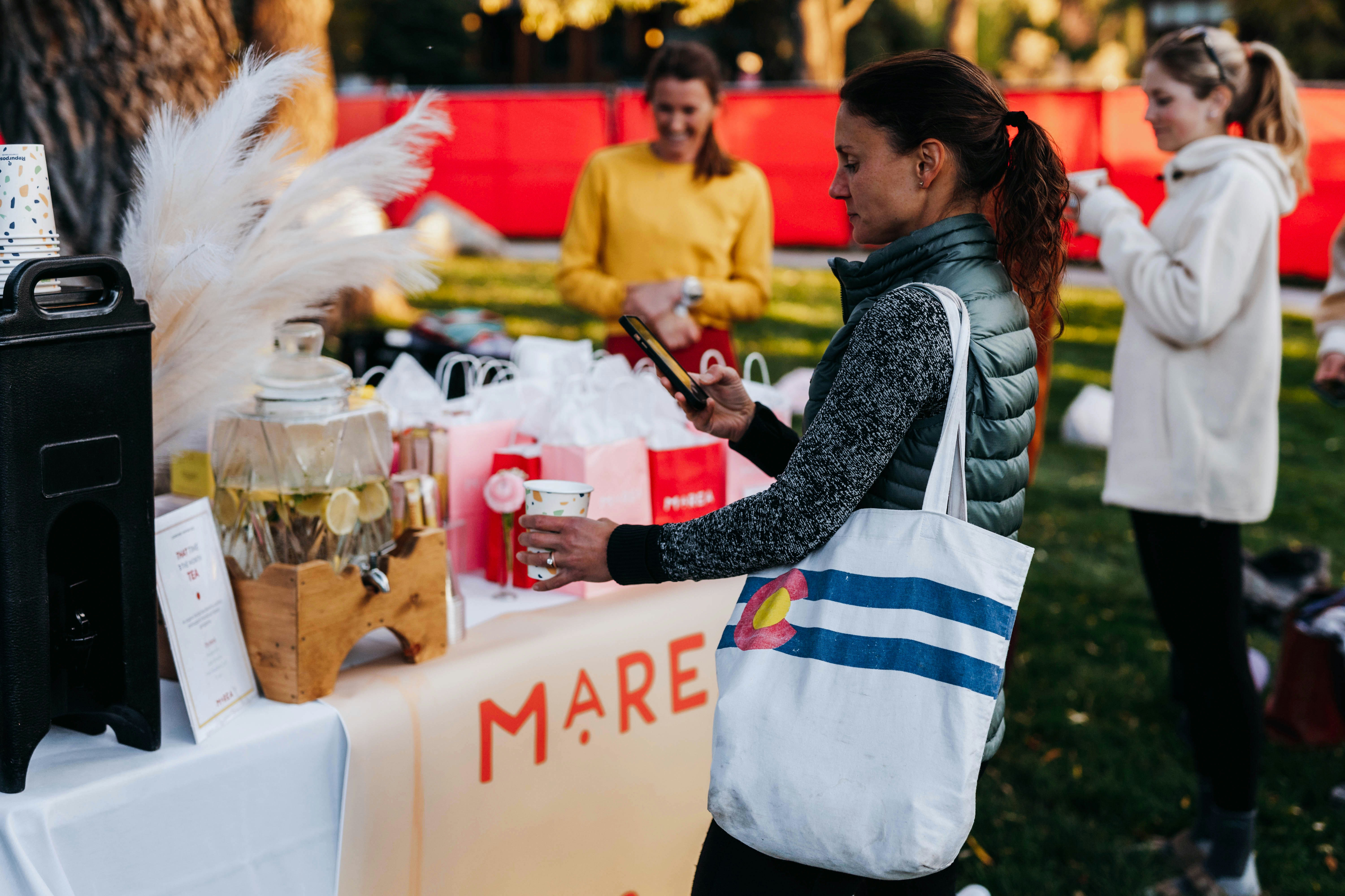 a woman standing next to a table with a bag on it, Witness the beauty of connection as a group of like-minded women unites, embracing the opportunity to forge new friendships and cultivate a nurturing community.