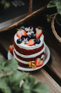 A vibrant red velvet cake topped with cream cheese frosting and fresh strawberries on a rustic wooden table