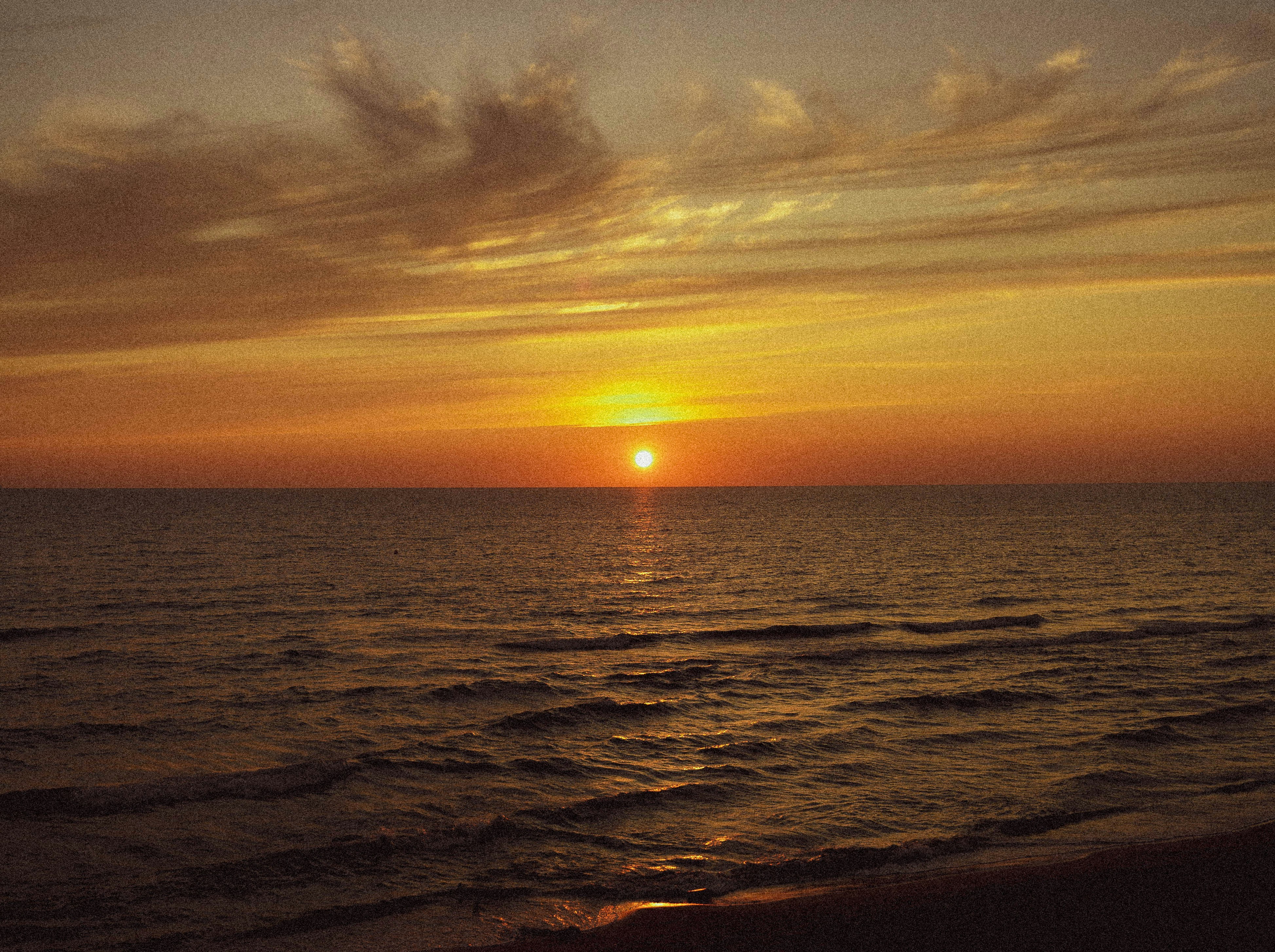 the sun is setting over the ocean on a cloudy day