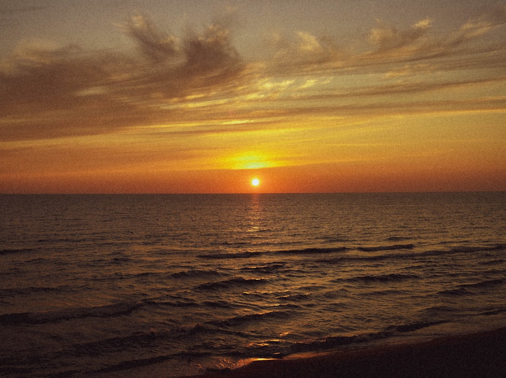 the sun is setting over the ocean on a cloudy day