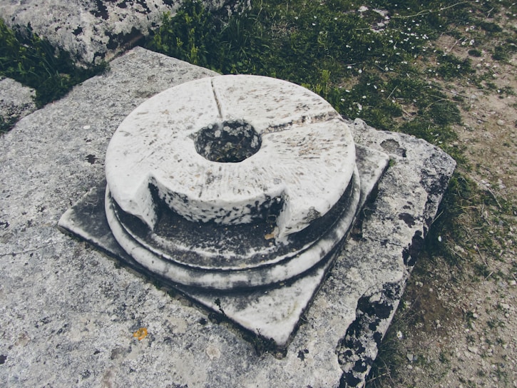 A weathered stone artifact partially buried in rich soil, surrounded by fallen leaves.