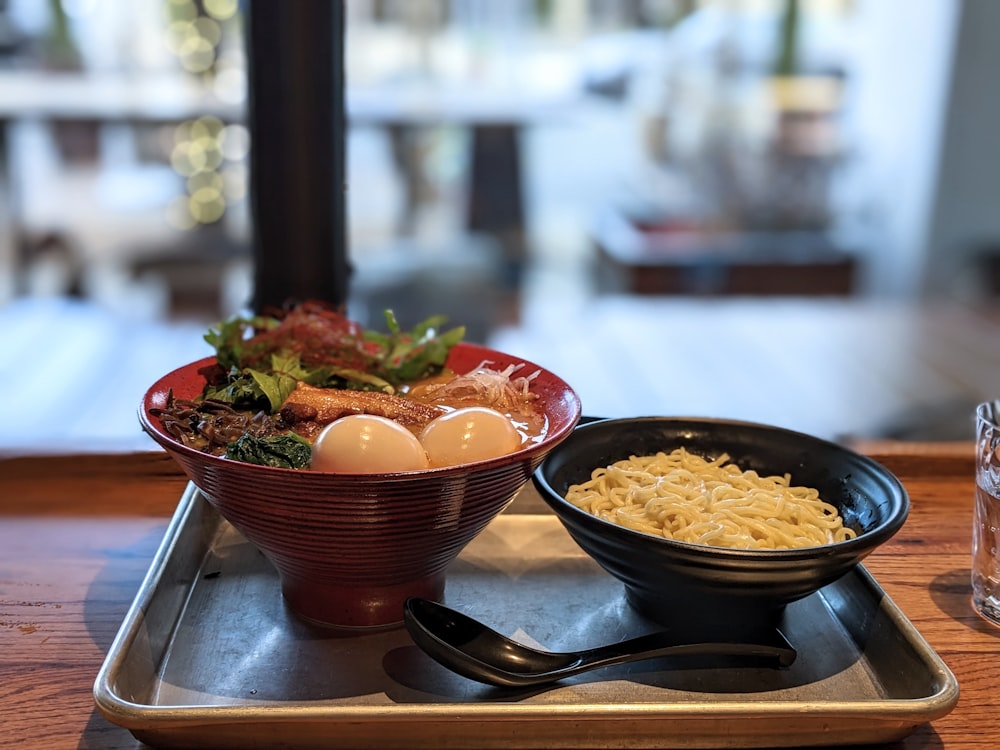 a bowl of noodles and a bowl of eggs on a tray