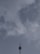 A tall telecommunications tower extends upwards into a cloudy sky, with a few clouds scattered around, and features a metal structure with antennas.