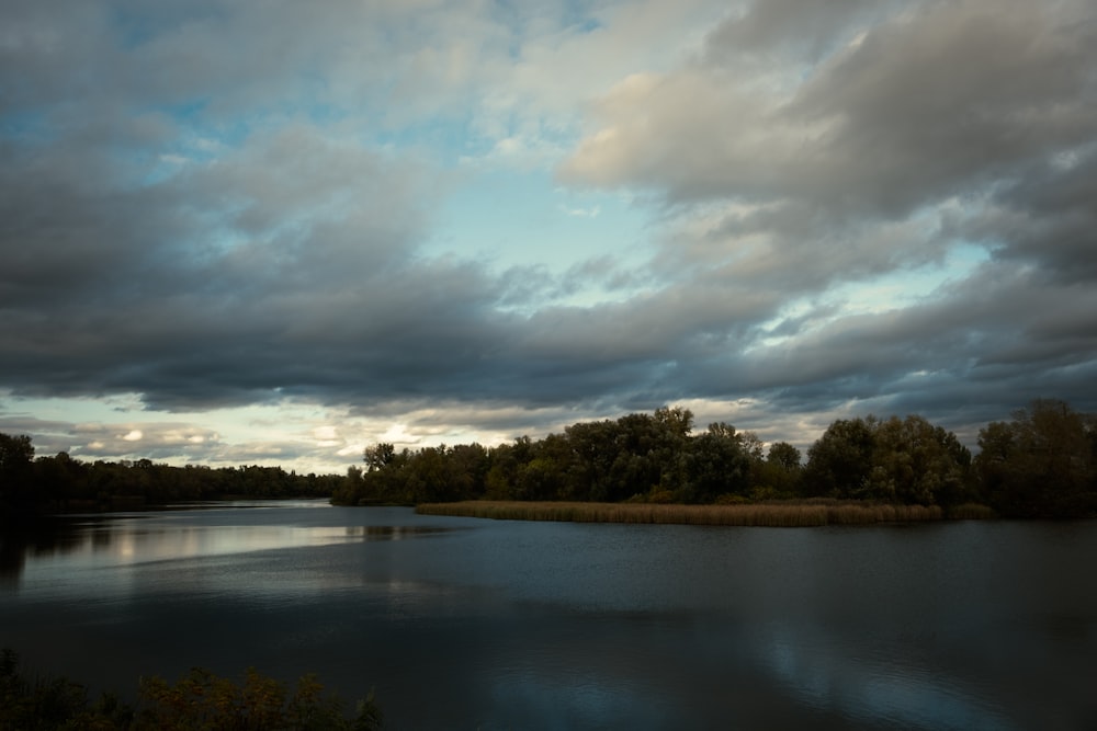 a body of water surrounded by trees under a cloudy sky