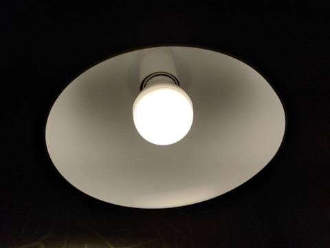 Close-up of a ceiling light fixture with a round white bulb emitting bright light. The fixture has a white inner surface creating a contrast against the dark background.