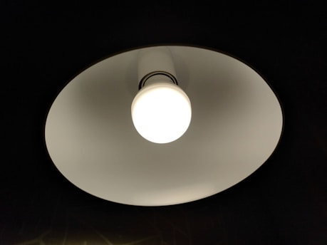 Close-up of a ceiling light fixture with a round white bulb emitting bright light. The fixture has a white inner surface creating a contrast against the dark background.
