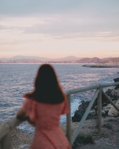 a woman in a pink dress looking out at the ocean