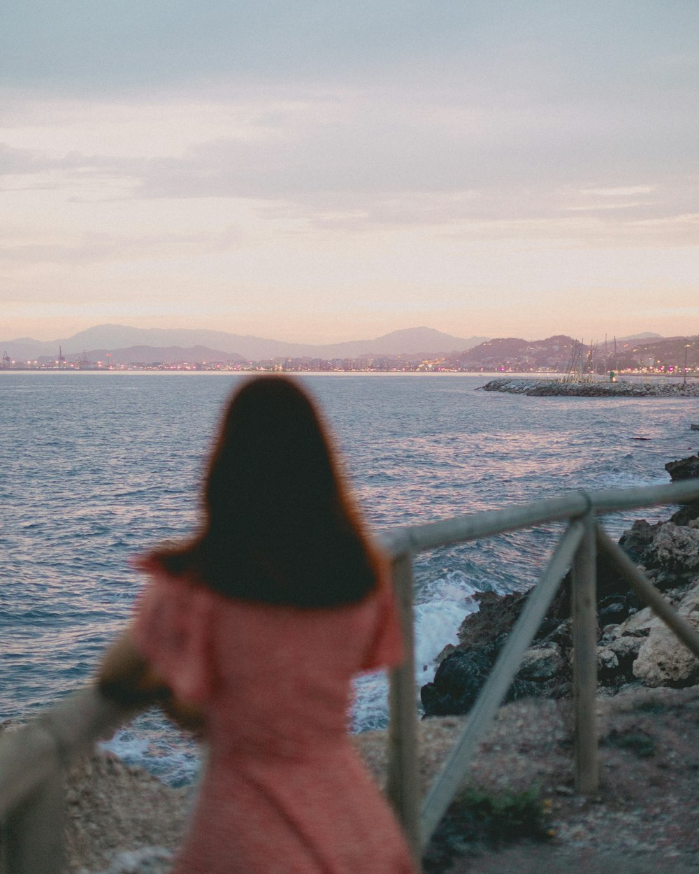 a woman in a pink dress looking out at the ocean