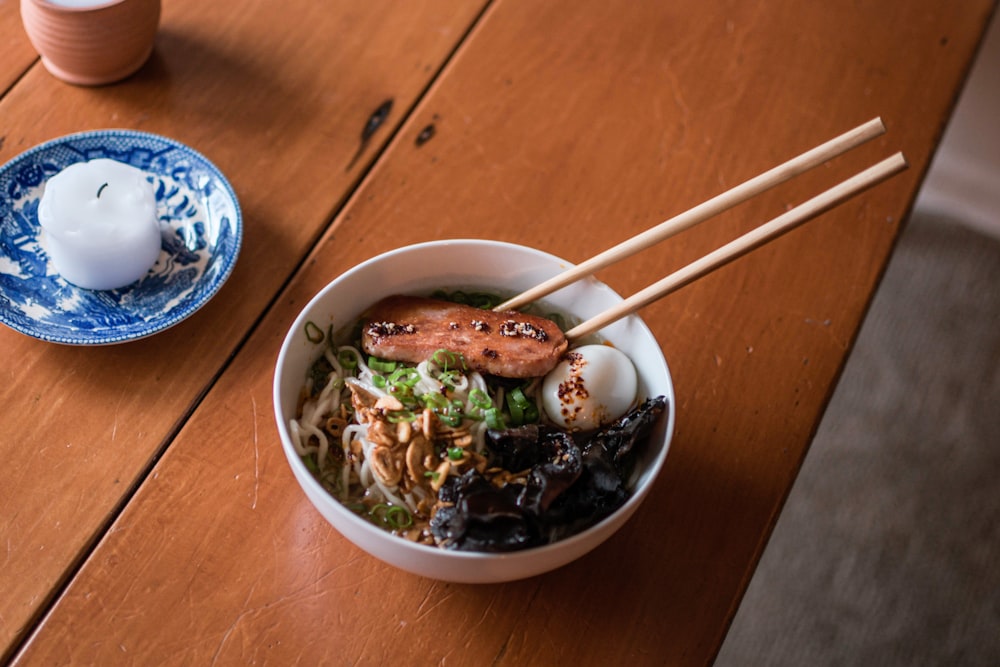 a bowl of food with chopsticks on a wooden table