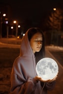 a woman in a hooded jacket holding a glowing moon