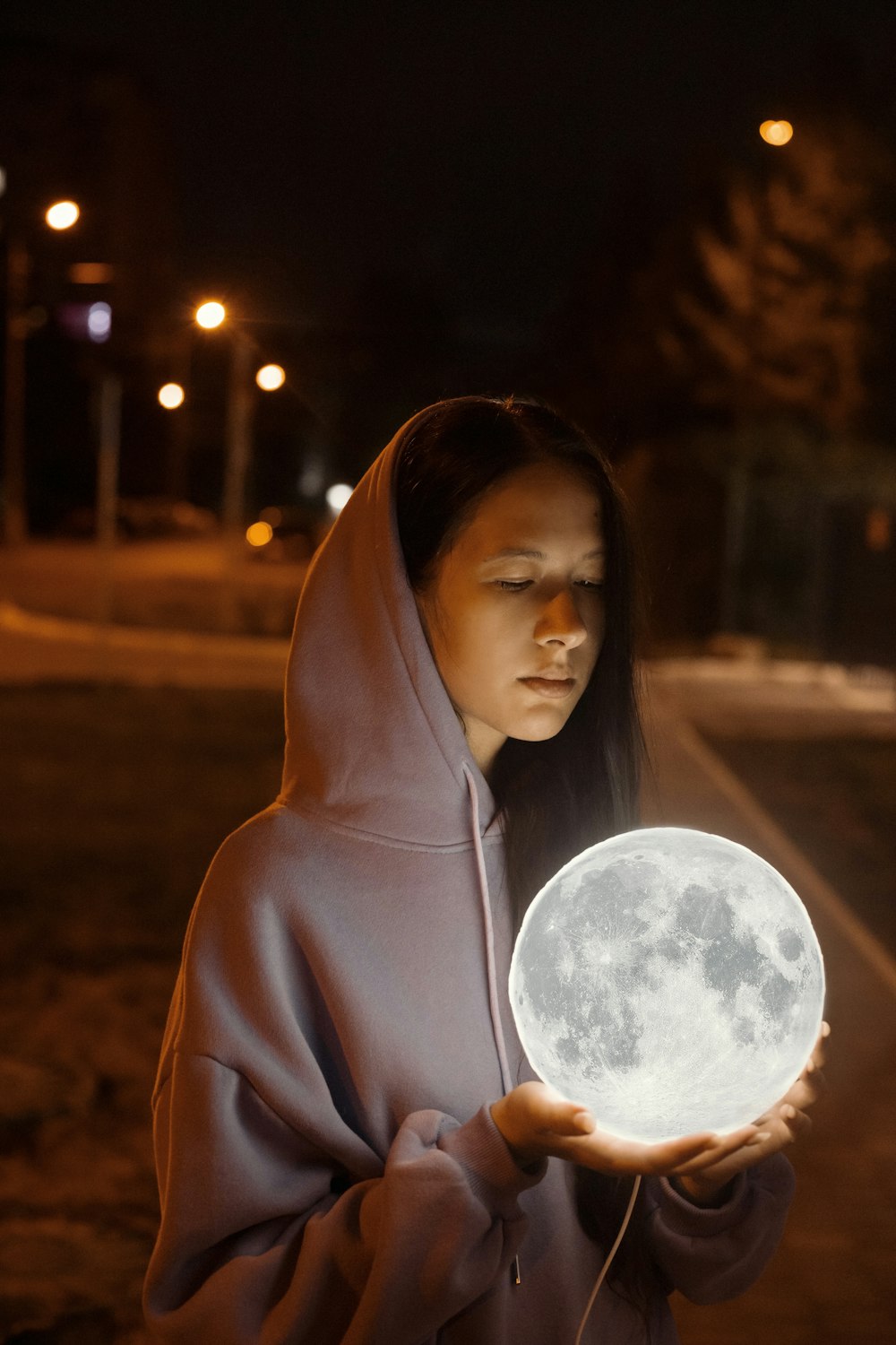a woman in a hooded jacket holding a glowing moon