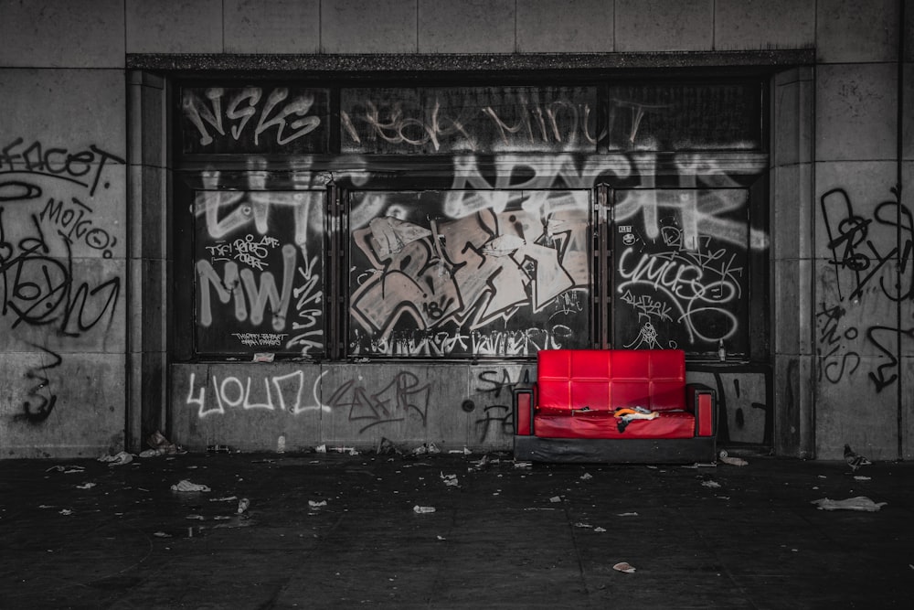 a red couch sitting in front of a window covered in graffiti