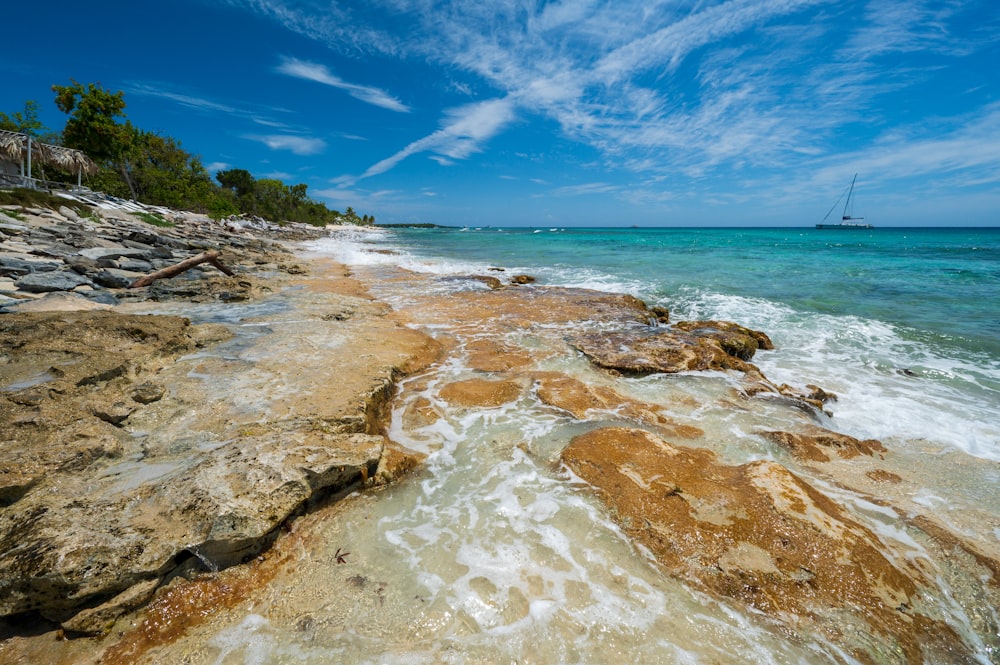 a rocky beach with a sailboat in the distance