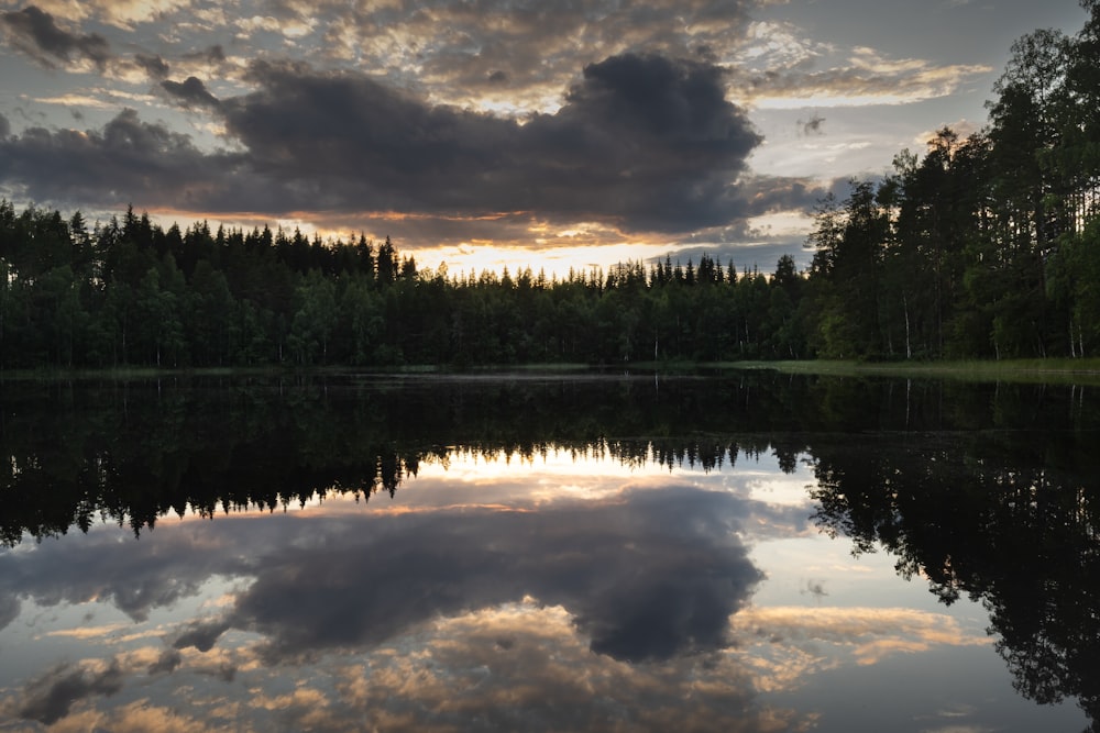 a lake surrounded by trees with a sunset in the background