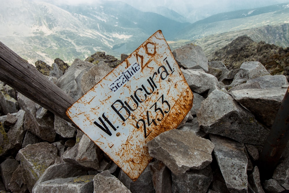 a rusty sign sitting on top of a pile of rocks