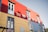 A brightly colored building features red, yellow, and blue corrugated panels. The structure includes several windows with white frames and small balconies. Signs with Spanish text are visible, adding a cultural element to the vibrant facade.