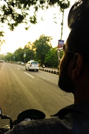 A cheerful driver on a motorcycle weaving through city traffic during sunset.