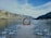 An outdoor wedding setup is situated by a lake surrounded by steep mountains. A circular floral arch forms a focal point at the end of an aisle lined with rows of white chairs.