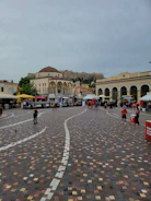 A bustling public square featuring durable soft stone flooring with people walking and sitting.