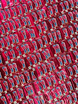 A repeated pattern of red packaged snacks with cartoon graphics and logos, neatly arranged side by side creating a colorful and symmetrical display.