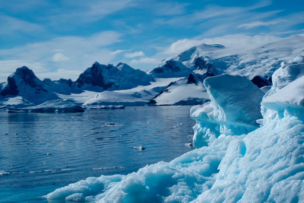 a large iceberg floating on top of a lake surrounded by snow covered mountains