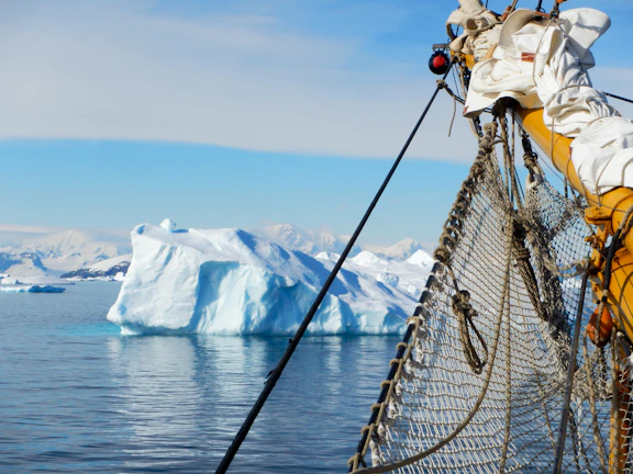 A majestic iceberg towering under a clear blue sky, with the expedition ship anchored nearby.