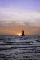 A sailboat silhouetted against a fiery orange and pink sunset over the ocean.