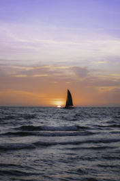 Alan Morgan steering his sailboat against a backdrop of a vibrant sunset over the ocean.