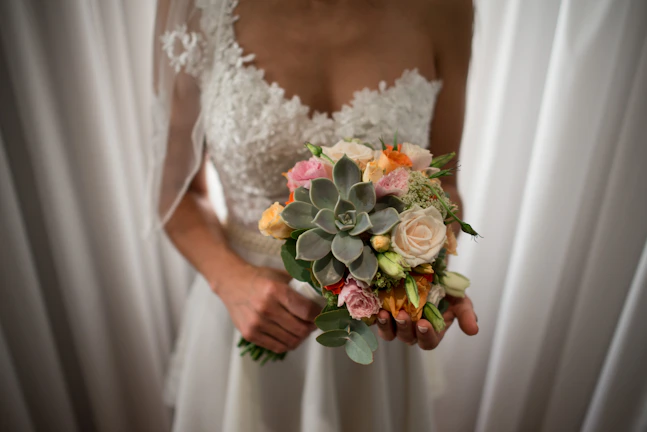 Bride holding a vibrant bouquet of mixed seasonal flowers against a backdrop of wedding decor.