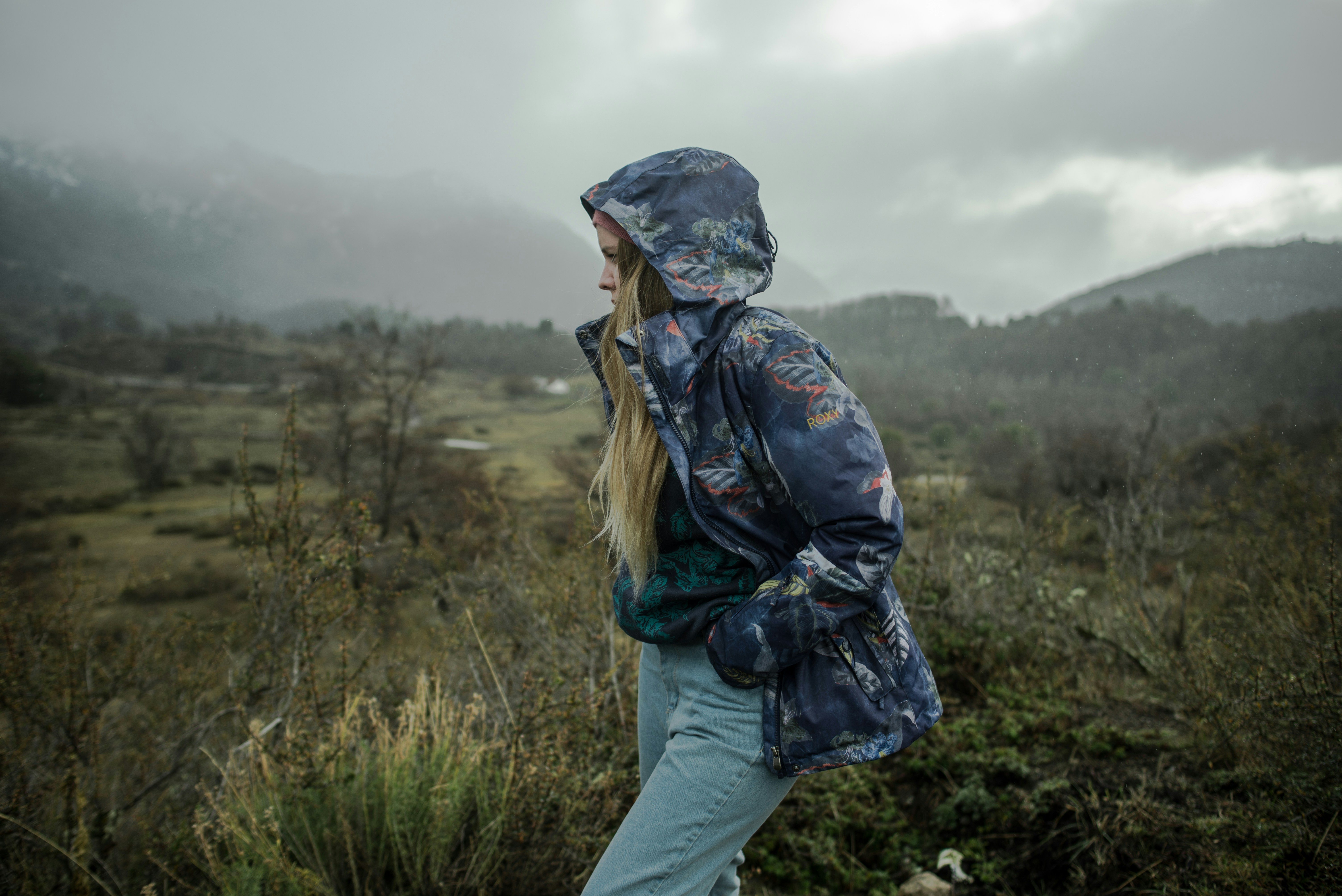 a woman standing in a field with mountains in the background
