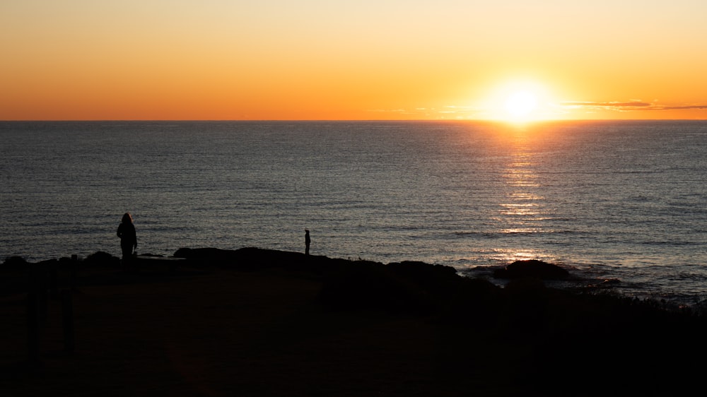 eine person, die auf einer klippe mit blick auf den ozean bei sonnenuntergang steht