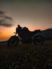 A single motorcycle silhouetted against a vivid orange and purple sunset over mountain peaks.