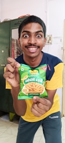 A smiling person packing Indonesian snacks into a shipping box at home.