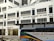 The image displays a large building with the signage 'Nanyang Academy of Fine Arts'. The structure is modern with multiple windows and the sign prominently displayed at the top. The ground level features a section labeled as NAFA Campus 2 with clear glass doors and an entrance. In the foreground, a bus with colorful stripes and the words 'Explore & Discover' on its side is present.