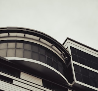 A modern architectural structure featuring curved and rectangular elements. The building exhibits a sleek design with large glass windows and metallic frames, showcasing contemporary urban architecture.