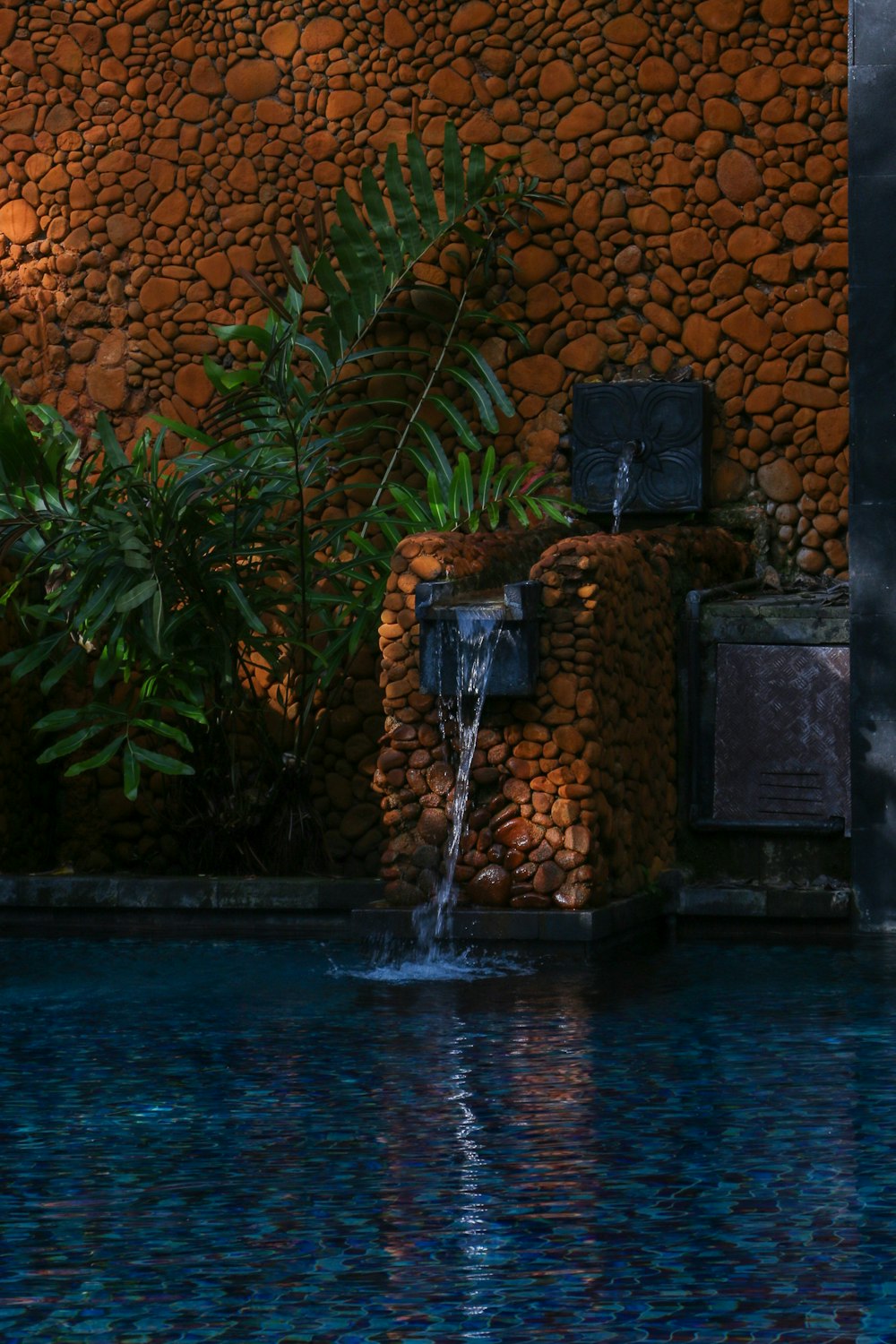 a pool with a waterfall next to a rock wall