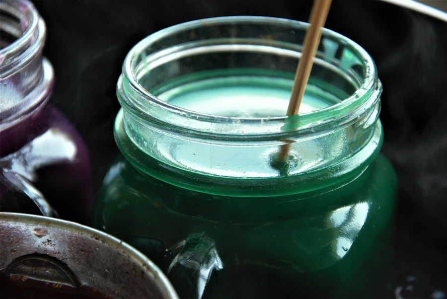 A wooden stick stirring sea green wax in a glass jar